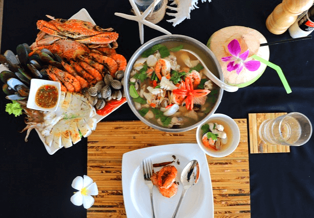 검정 식탁에 해물탕 한세트가 차려졌다. 은색 냄비에 해물탕이 가득하고, 주변 접시엔 꽃게구이, 새우구이, 조개구이가 가득하다.