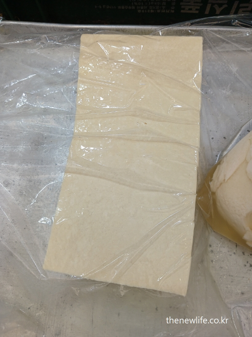 A large block of fresh tofu wrapped in plastic, displayed at a traditional Korean market- 전통시장에서 포장된 상태로 진열된 신선한 두부-고지혈증에 좋은 음식
