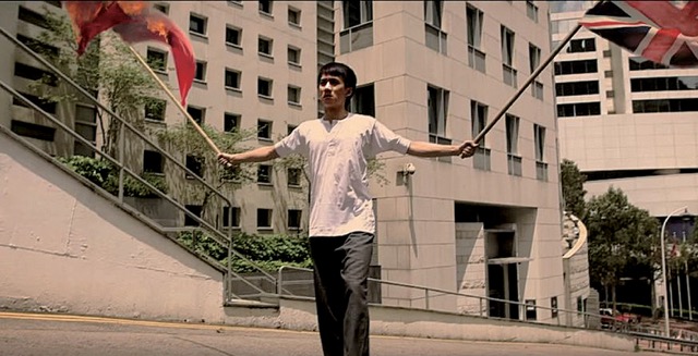 영화 《10년》에서 한 남성이 홍콩과 영국 국기를 양손에 든 채 도심을 걷는 장면. 국기 두 개 사이에서 갈등하는 그의 모습은 정체성의 혼란과 주체성 상실의 현실을 고스란히 드러낸다.