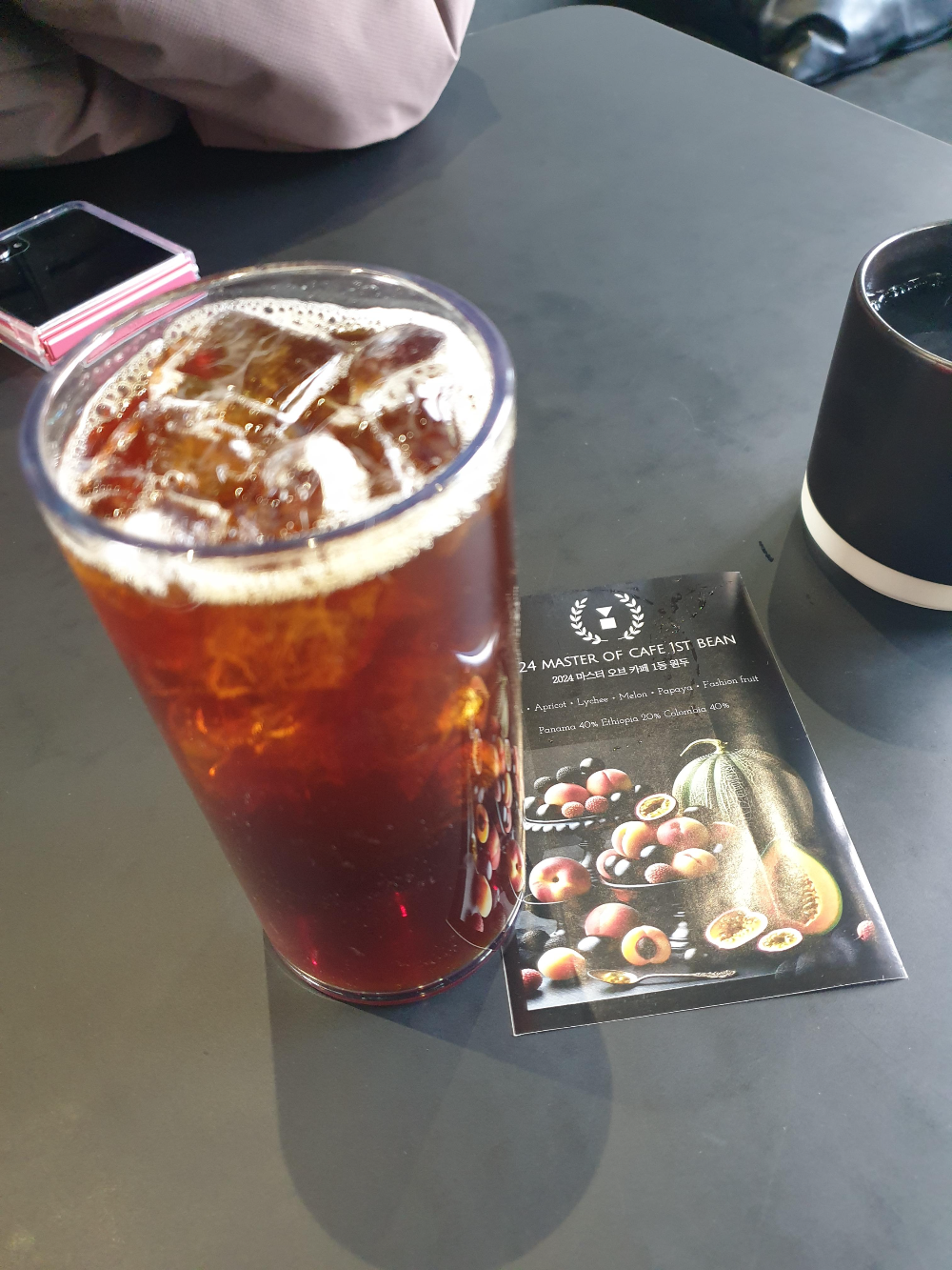 열대과일 그림이 있는 컵노트와 아이스커피가 테이블 위에 있다.