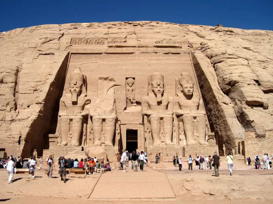 아부심벨 대신전 외벽에 조각된 람세스 2세의 좌상과 정문 앞을 걷는 관광객들 모습