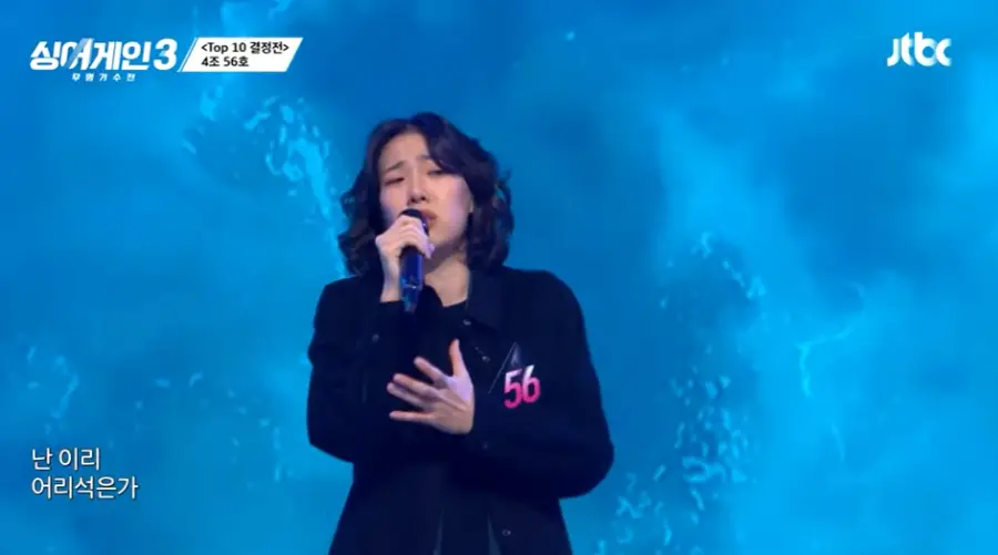 싱어게인 3-
파란배경 검은옷을 입은 56호가 슬픈 표정으로 검은 마이크에 대고 노래하는 모습