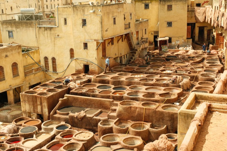 Overhead view of traditional leather tannery in Fes, Morocco, with workers and dye vats.