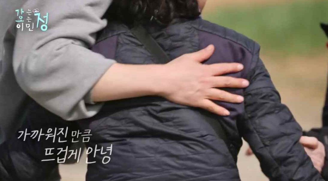 붐이 효자도 주민 아주미의 등을 감싸 안고 있는 뒷모습에 가까워진만큰 뜨겁게 안녕 자막이 있는 스틸컷