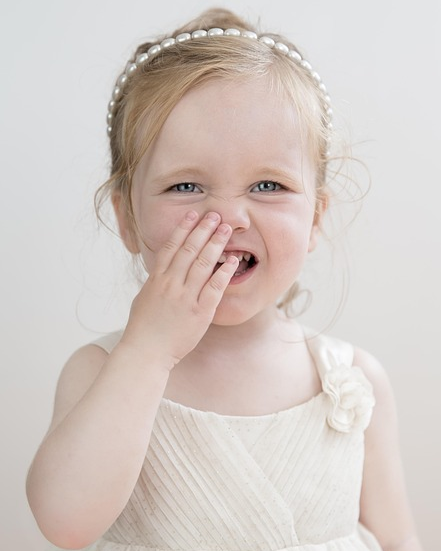 코를 만지며 웃고 있는 어린 여자아이 – 알레르기성 비염 증상을 간접적으로 보여주는 모습