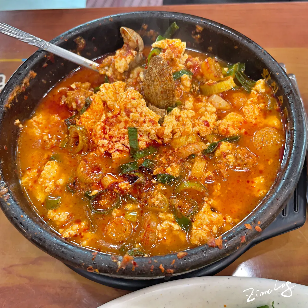 화심 순두부찌개의 모습으로 찌개를 숟가락으로 드니까 순두부, 다진고기, 바지락이 함께 들어 있는 것을 숟가락으로 떠서 있음
