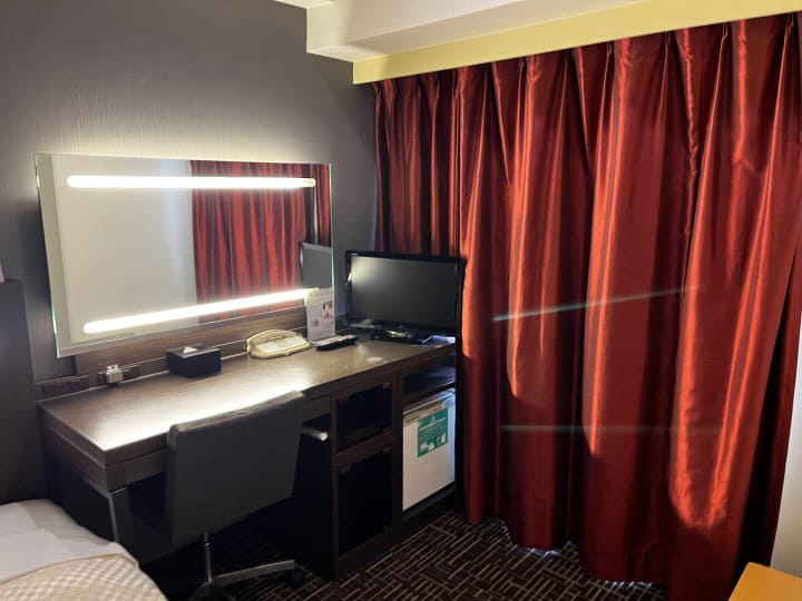 책상에 조명 거울과 전화기, 티비가 있음