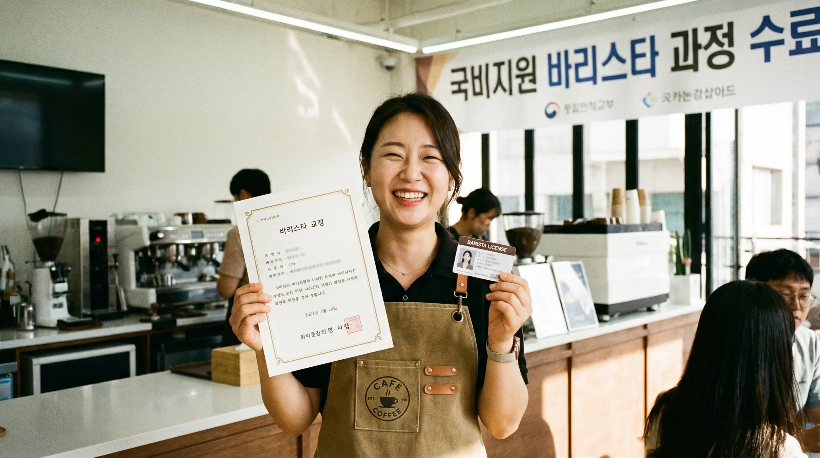 국비지원 과정을 수료하고 바리스타 자격증을 손에 든 채 밝게 웃으며 카페 앞치마를 두른 수강생의 모습