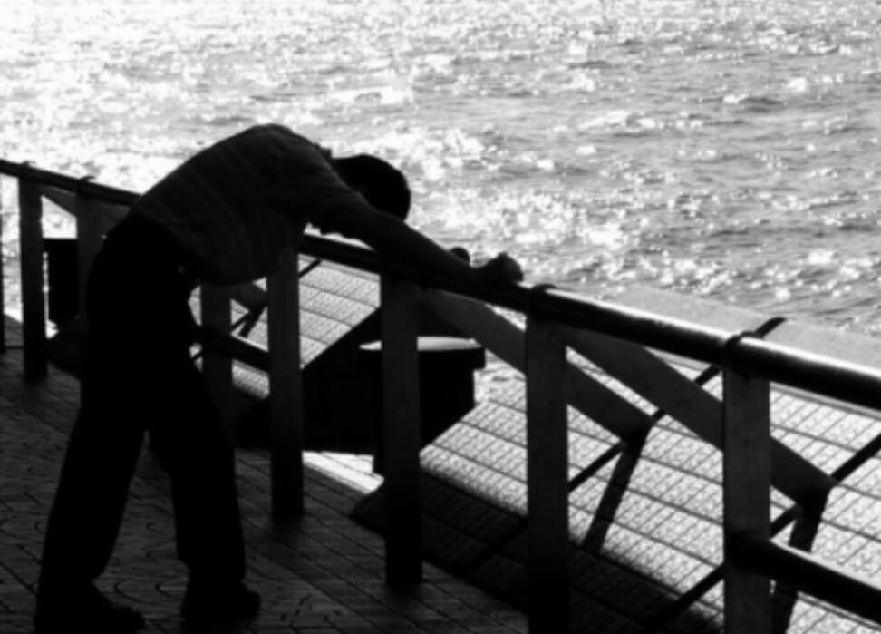 남자가 바다 앞에서 고개를 숙이고 좌절하고 있다