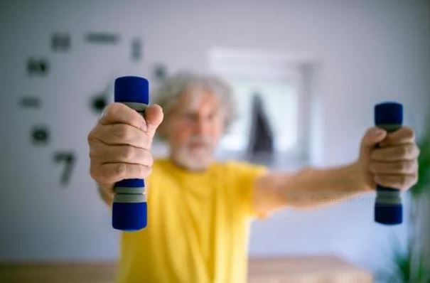 근력운동 적정 빈도 - 중년 남성이 가벼운 덤벨로 홈트레이닝하는 모습 via canva