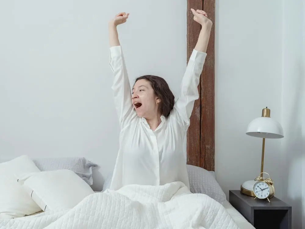 침대에 앉아 아침에 자연스럽게 하품하며 가볍게 기지개를 켜는 여성의 모습