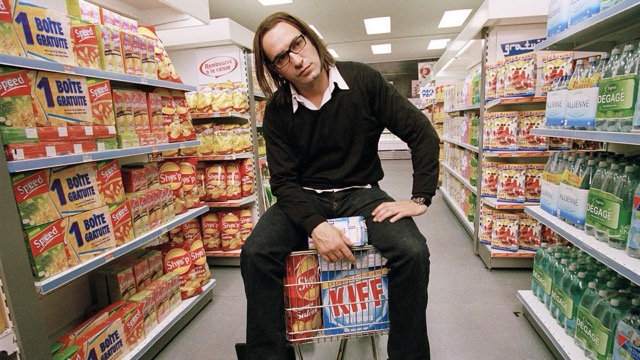 영화 《99 프랑》에서 광고 천재 옥타브가 슈퍼마켓 진열대 사이에 앉아 있는 장면. 넘쳐나는 상품들 속에서 그는 냉소적이고 무기력한 표정으로 자본주의 소비의 허무함을 대변한다.