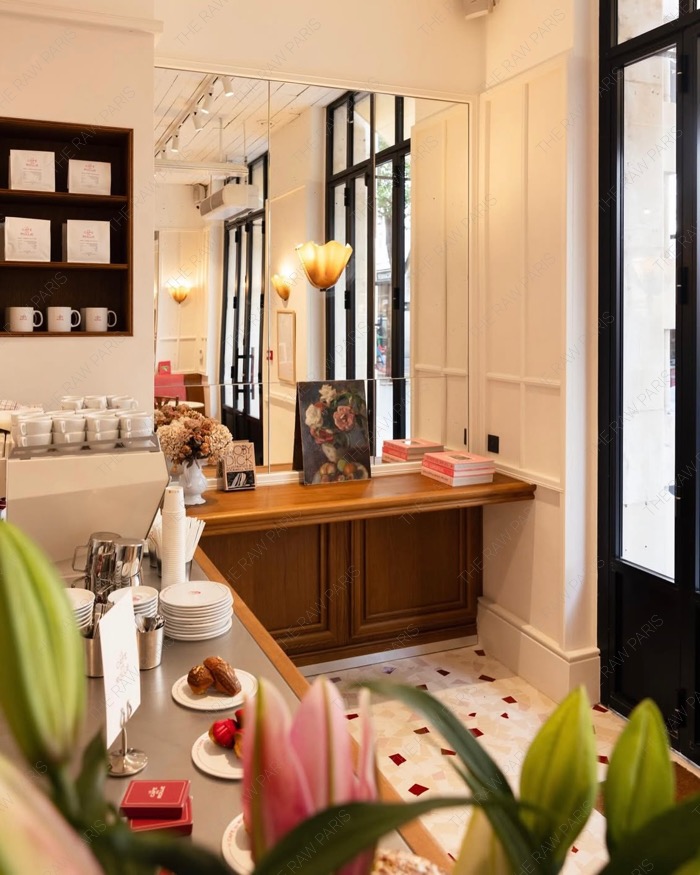 Wooden espresso bar inside Le Cafe en Rouje with a vase of pink lilies and cakes under glass domes⁠