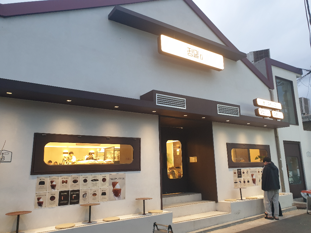 흰색 벽면에 우드 창틀 그리고 외부 테이블과 좌석이 있는 정밀 외부