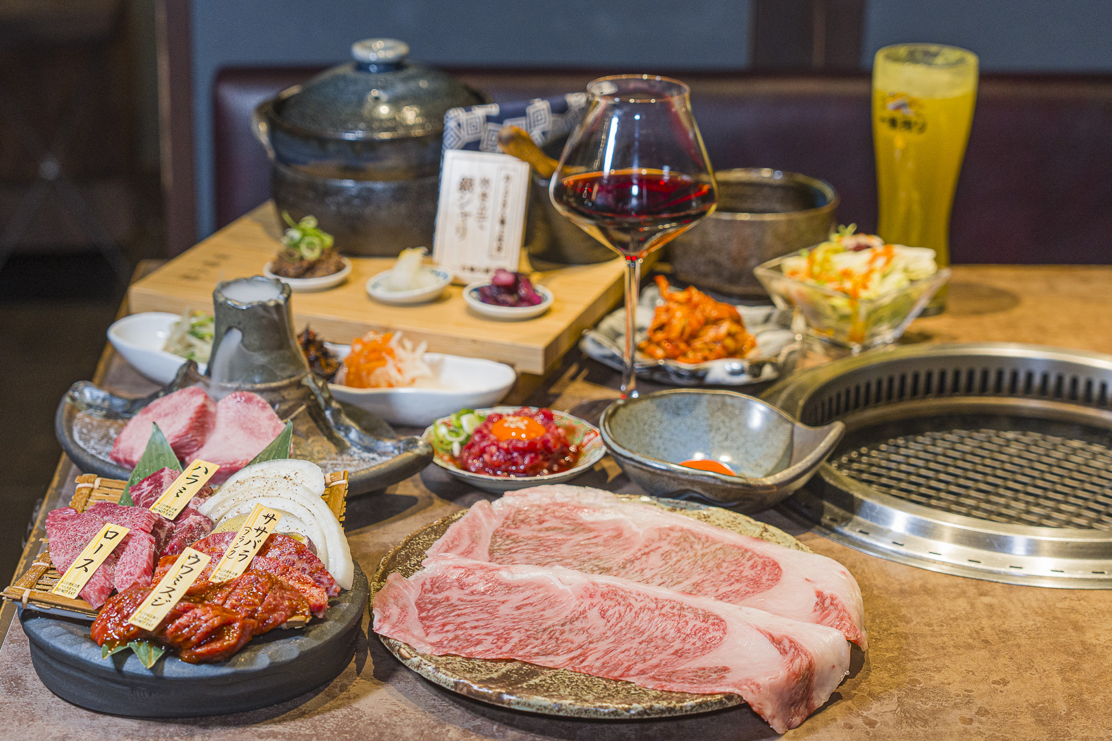 Yakiniku Ichiba Koji, Kiyamachi: marbled beef and labeled assorted cuts, side dishes and drinks beside a tabletop grill.