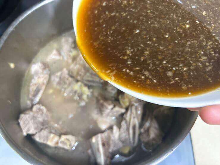 갈비와 육수가 담긴 냄비에 갈비 양념을 넣고 있는 사진이다.