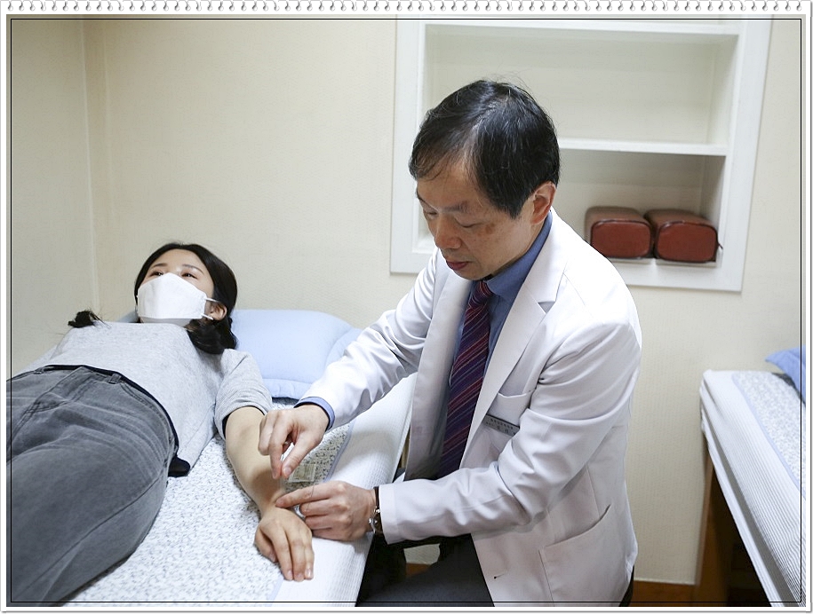 누워있는 환자의 손등에 침을 놓고 있는 남성 한의사의 모습