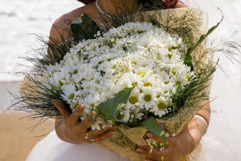 A close-up of a bride holding a lush bouquet of white daisies on her wedding day.