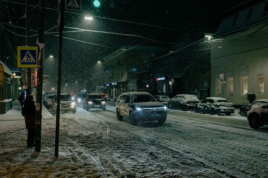 Urban street scene at night with snow, cars, and streetlights illuminating the roadway.