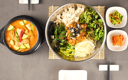 검정 뚝배기에 구수한 황토색 된장찌개가 있다. 고추와 애호박, 두부가 가득하다. 옆에는 된장비빔밥이 있는 양푼이 있다.