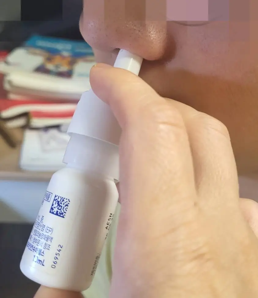 오트리빈을 왼쪽 콧구멍에 넣고 두번째 손가락과 세번째 손가락으로 펌프를 누르고 있는 옆모습