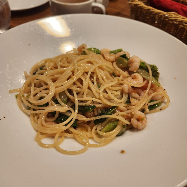 흰 접시에 담긴 오일 파스타. 새우와 시금치가 보인다.