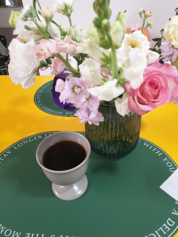 노란 테이블에 꽃병과 추출된 커피가 함께 놓여 있다.