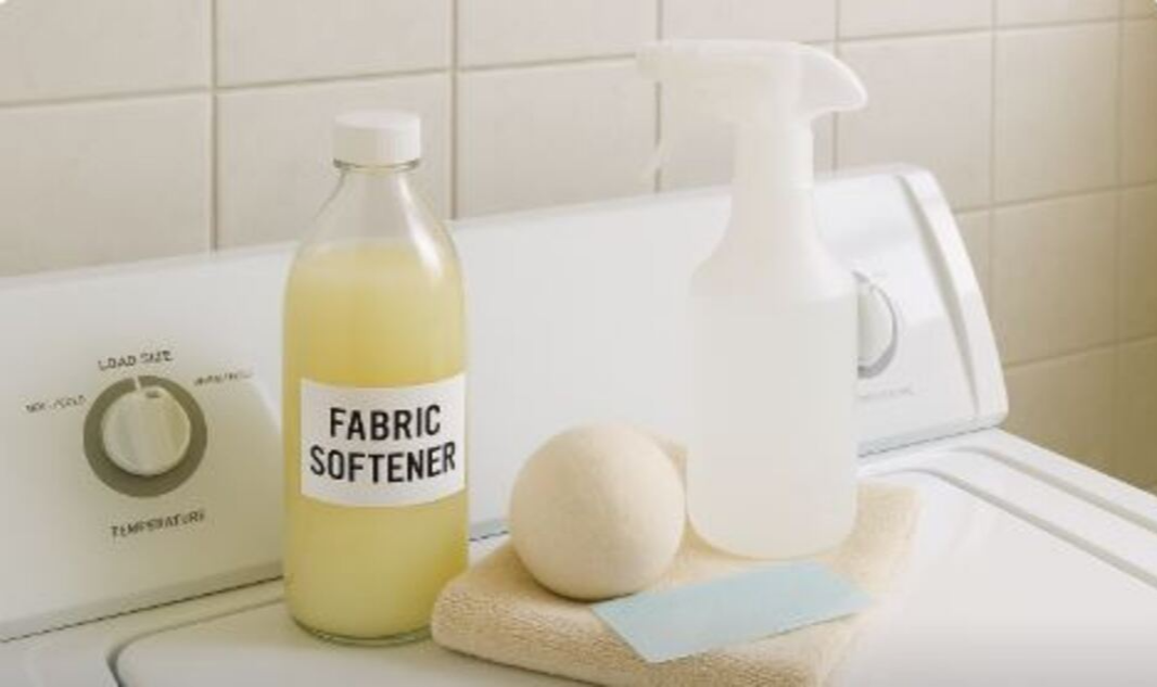 세탁기위에 섬유유연제와 섬유볼, 접혀진스웨트가 있는 사진