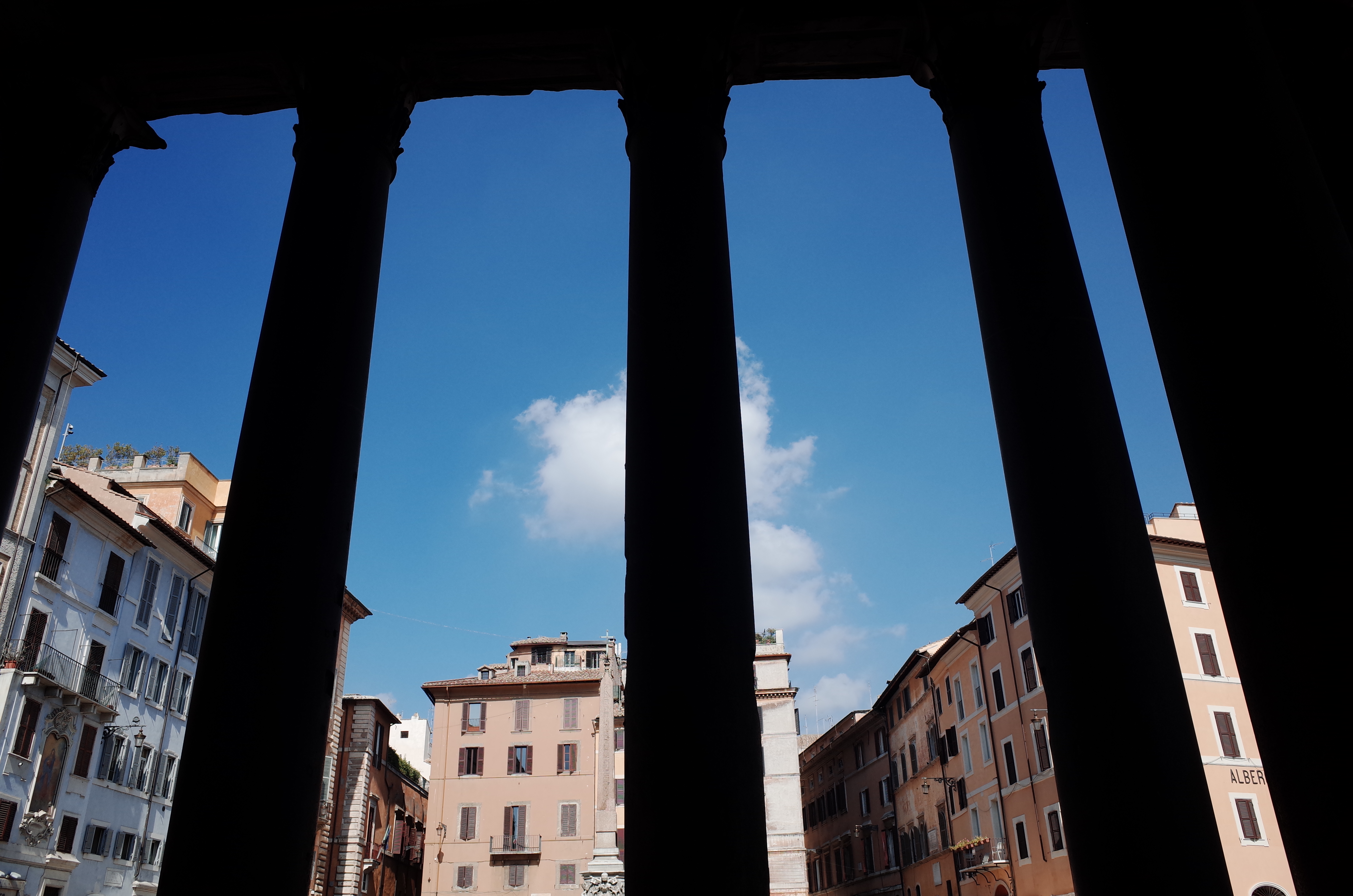 판테온의 거대한 기둥 사이 실루엣 너머로 펼쳐진 로마 광장과 푸른 하늘