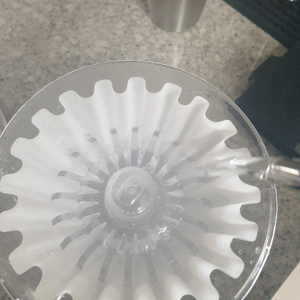 칼리타 드리퍼 위에 필터가 꽃혀 있고 린싱 보조 도구가 꽃혀 있다. 드립포트에서 나오는 불줄기가 보인다.