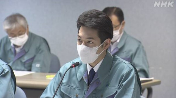 한 남성이 마스크를 쓰고 마이크 앉아 있다. 앞에는 마이크가 있다