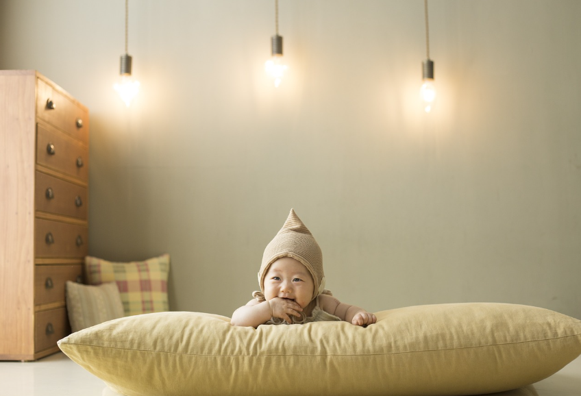 노란 모자를 쓰고 노란 쿠션위에 엎드려 있는 아기