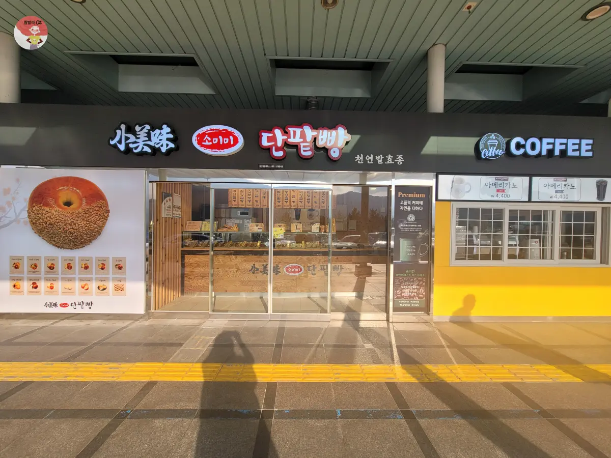 소미미 단팥빵과 커피를 판매하는 현대적인 베이커리 카페의 외관. 한쪽에는 단팥빵 이미지와 다양한 빵 사진이 있고, 중앙에는 유리문과 나무 인테리어가 보인다
