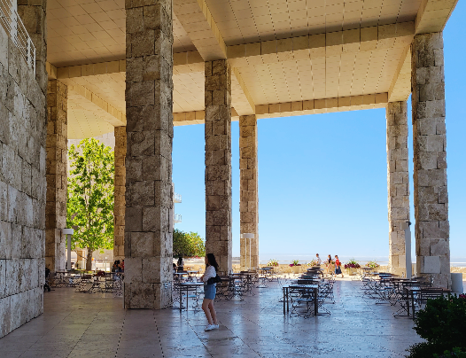 가든 테라스 카페. 의자와 테이블이 그늘 안쪽으로 여러 개 마련되어 있다. 굉장이 높은 기둥 앞으로 내가 지나가고 있다. 