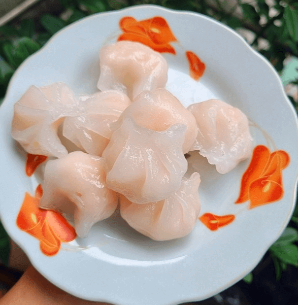 하얀 접시에 새우만두 8개가 있다. 만두피는 하얗고 속은 분홍색 새우가 들어갔다.