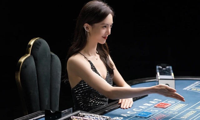 영화 《노 모어 베츠》에서 매혹적인 카지노 딜러가 카드를 돌리는 순간. 화려한 조명과 미소 뒤엔 사람들의 탐욕과 착취가 교묘하게 엮여 있다.