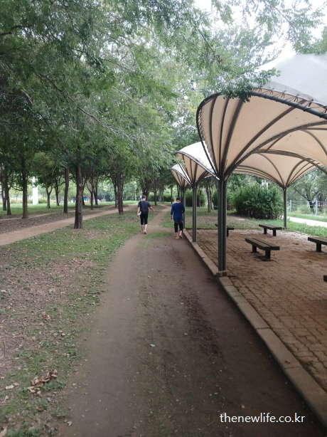 광나루 한강공원 그늘 쉼터 옆 흙길을 맨발로 걷는 중년 남녀의 모습 &ndash; 자연 속 휴식과 운동을 할수 있는 서울 맨발 걷기 좋은 장소