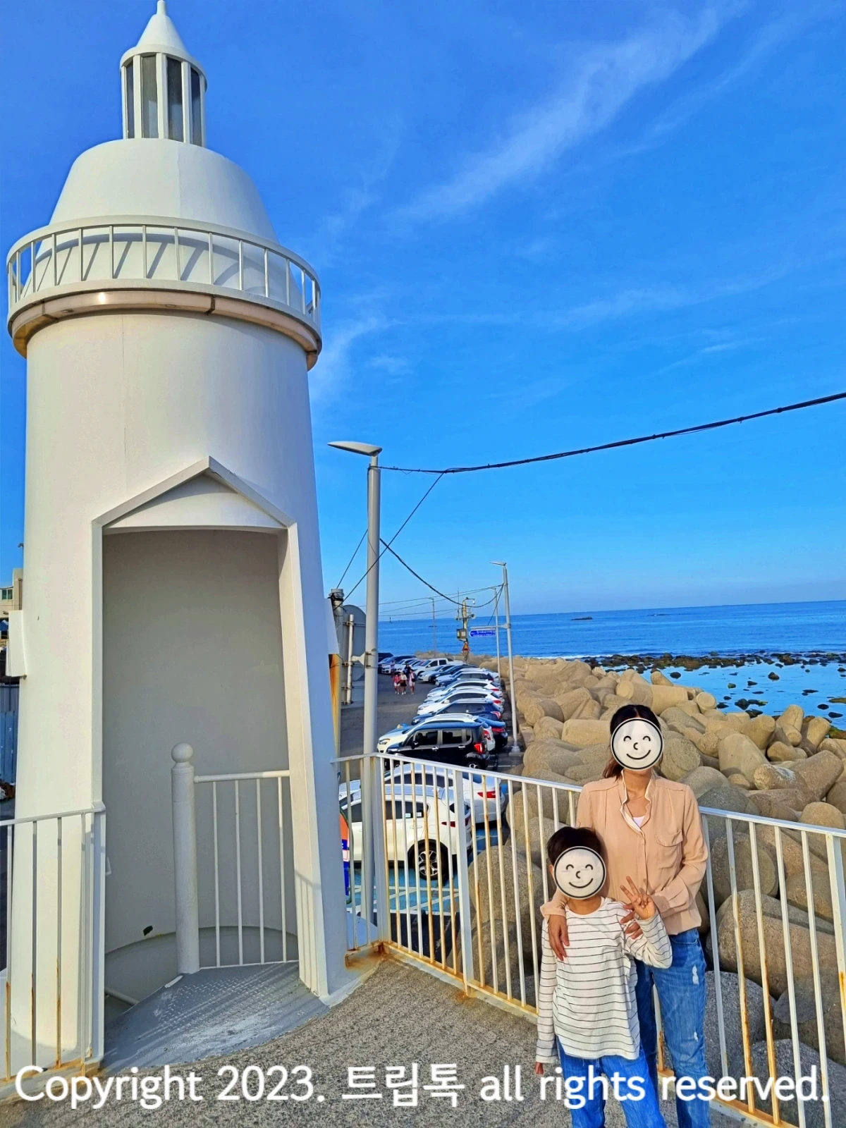 왼쪽에 하얀 등대가 있고 오른쪽에 두사람이 서있다