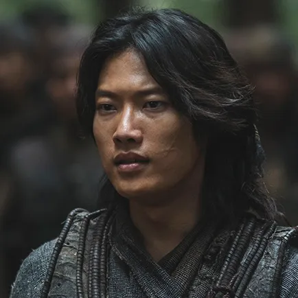 병사를 배경으로 20대 남성이 긴머리를 뒤로 묶고 검은 가죽 갑옷과 무복을 입고 있는 아라문의 검 달새 캐릭터