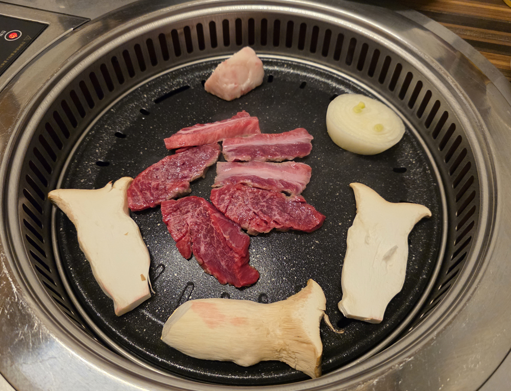 불판 위에서 굽기 시작한 한우 부위와 양파&amp;#44; 새송이버섯이 함께 올려진 모습
