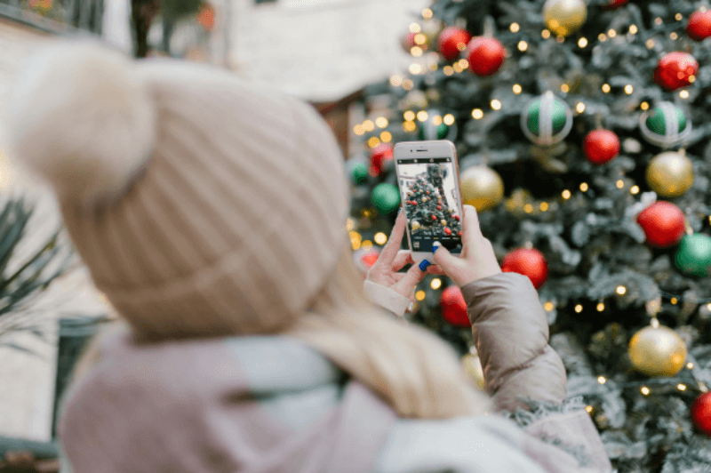 겨울모자를 쓴 소녀가 휴대폰을 들고 크리스마스 트리 사진 찍는 장면