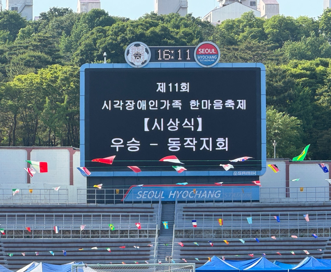 이미지설명: 제11회 시각장애인가족 한마음축제 시상식이라고 쓰여진 전광판 위에 우승-동작지회라고 떠있다.