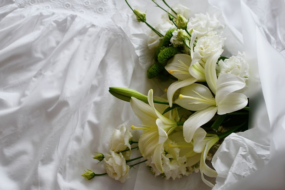 A bouquet of white lilies and carnations placed on delicate white fabric, perfect for wedding themes.