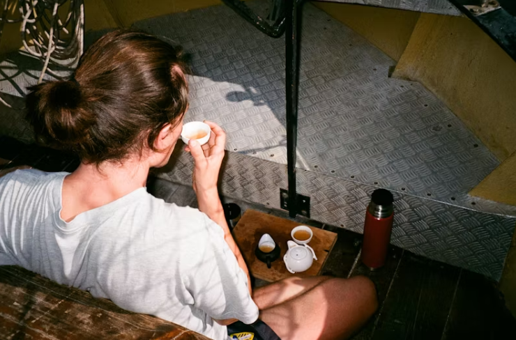 조용한 아침, 계단 옆에 앉아 차를 마시는 사람의 모습. 티포트와 찻잔이 놓인 나무 쟁반, 따뜻한 햇살이 비치는 편안한 분위기.