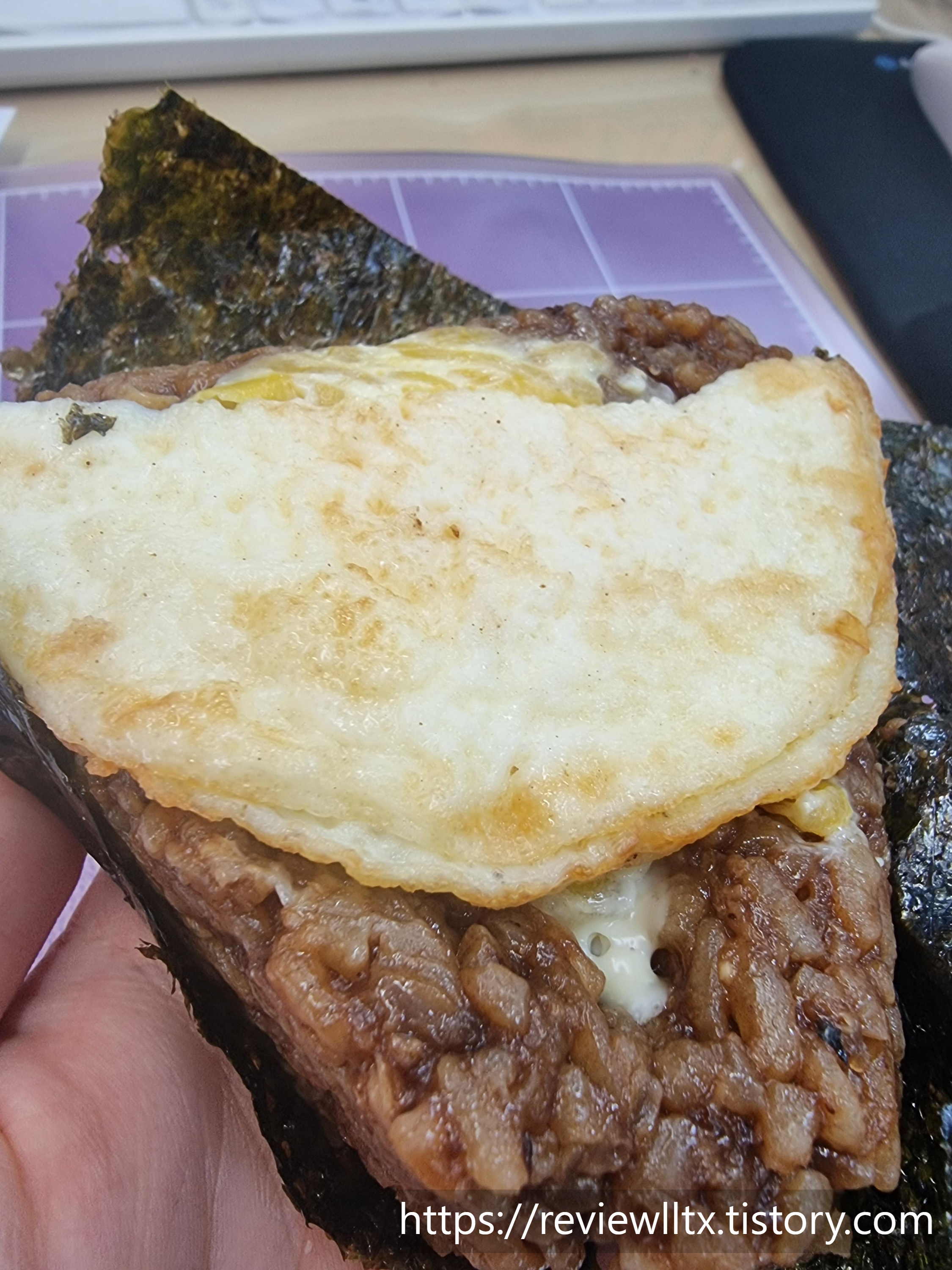 삼각김밥 김의 한 쪽을 제거한 사진&#44; 짜장밥 위에 단무지마요&#44; 계란후라이 순서대로 놓여있다.