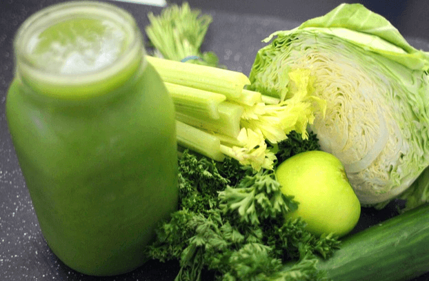 작은 유리병에 녹색의 양배추즙이 가득 들어있다. 옆에는 반으로 잘린 양배추와 샐러드가 있다.