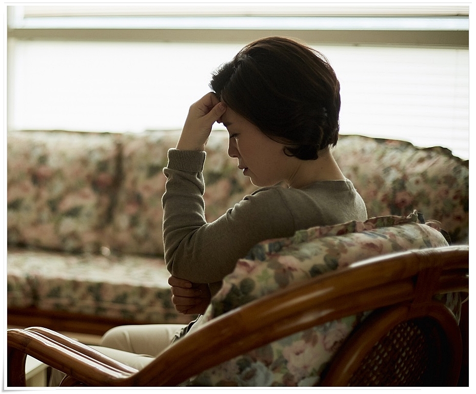 한 손으로 이마를 짚은 채 다소 힘든 표정을 짓고 있는 중년 여성의 모습