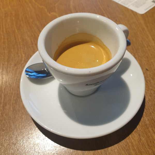 에스프레소 컵과 스푼이 보인다. 우드 테이블 위에 올려져 있다.