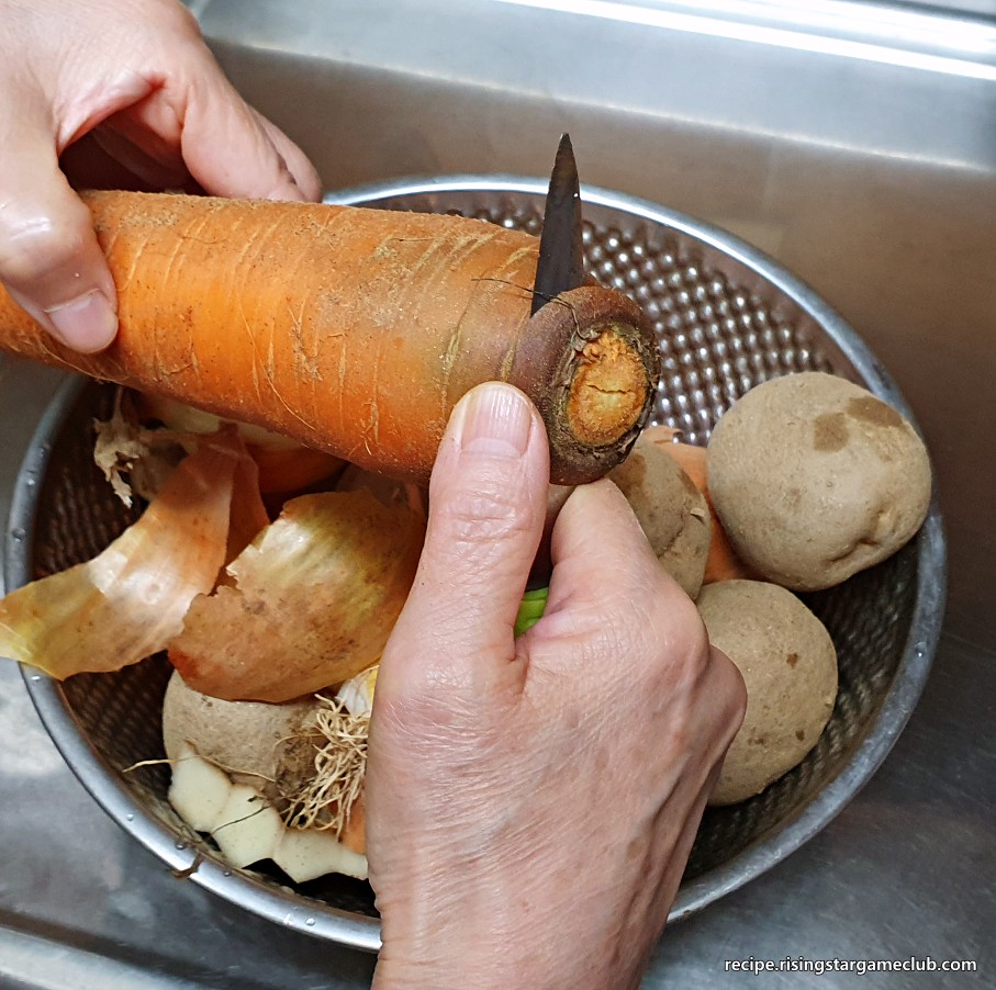 돼지고기 카레라이스에 들어갈 당근의 잎파리가 나는 부분을 제거하는 사진