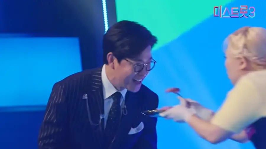 미스트롯3- 파란색배경 노란색 웃옷 입은 수빙수 출연자가 검정색 옷을 입은 사회자 김성주에게 회를 먹이는 모습